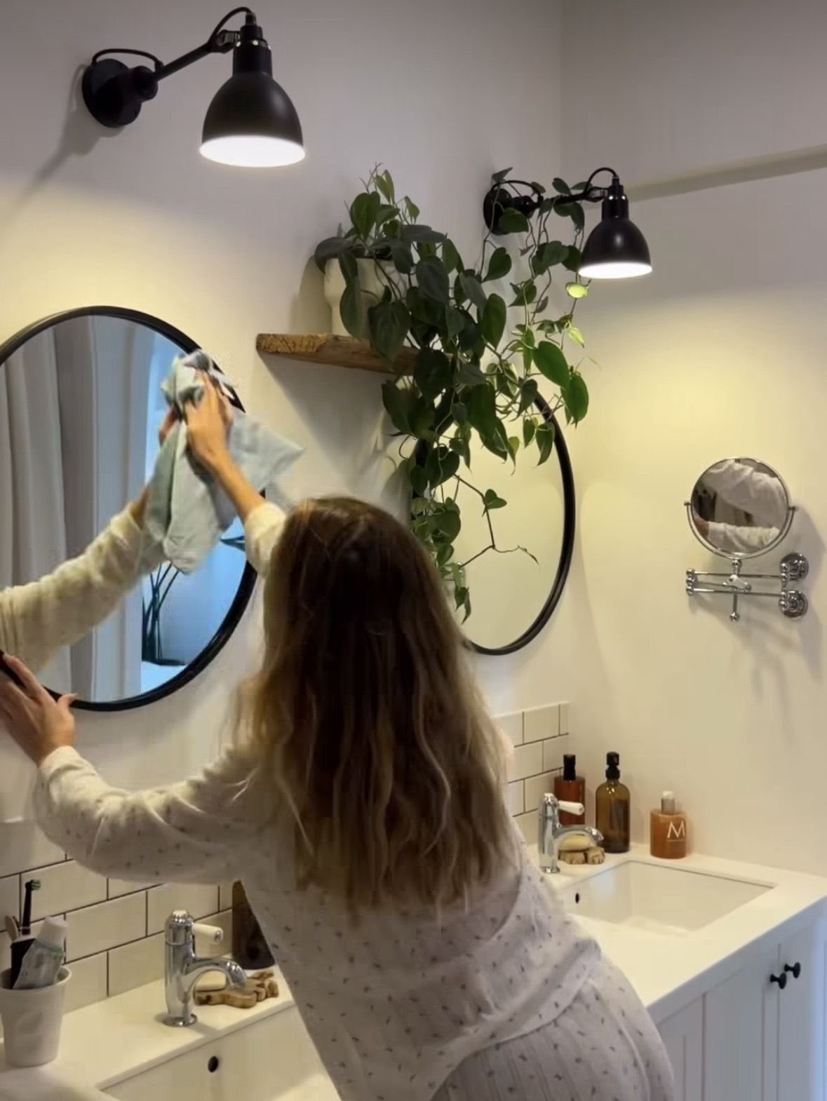 6 Aesthetic Cleaning Videos That Make Organizing Look Like Art 3 A person wiping a round bathroom mirror with a blue cloth in a bright room.