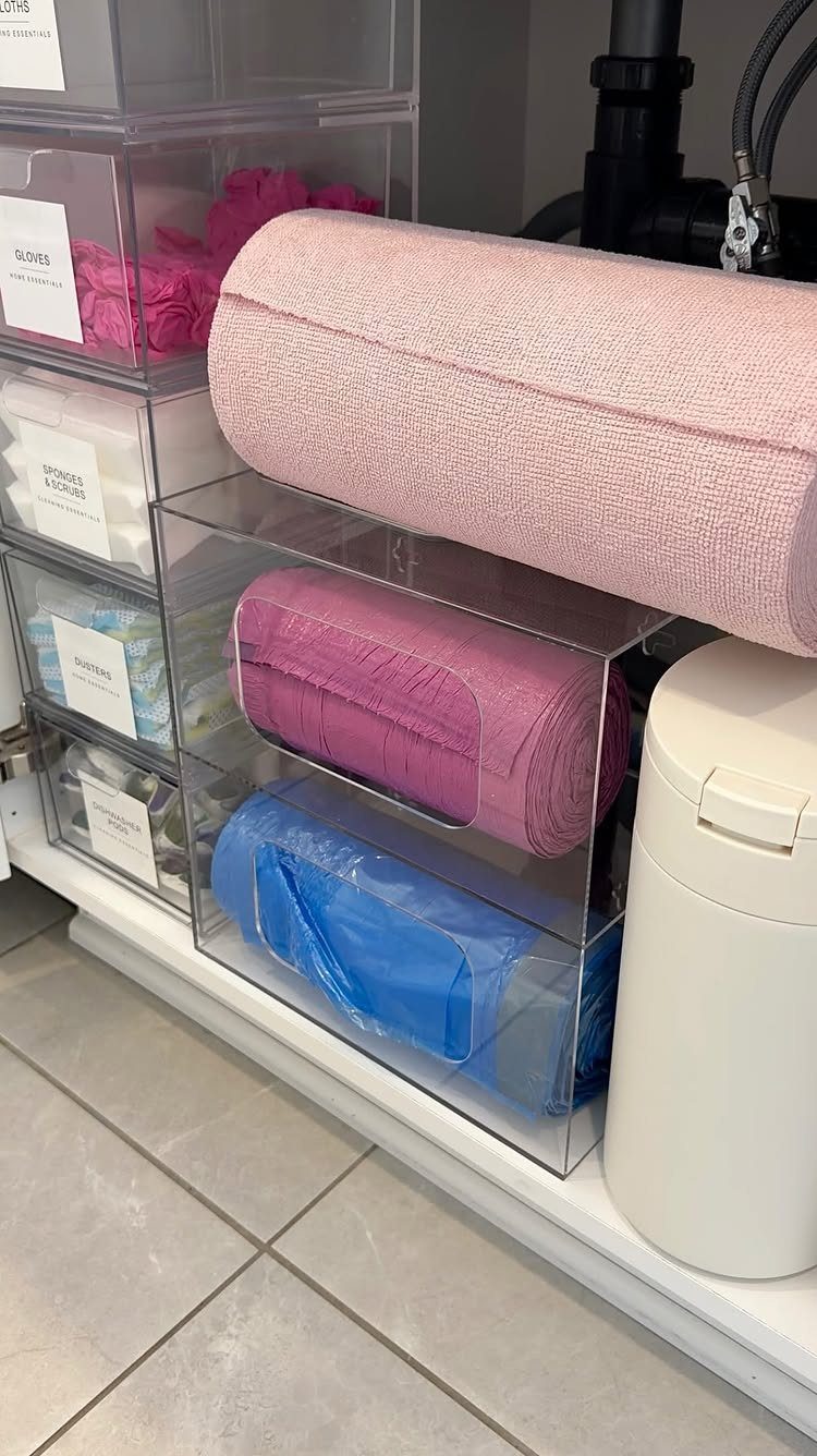 6 Aesthetic Cleaning Videos That Make Organizing Look Like Art 1 Clear acrylic organizers holding rolled pink and blue cleaning cloths on a white shelf.