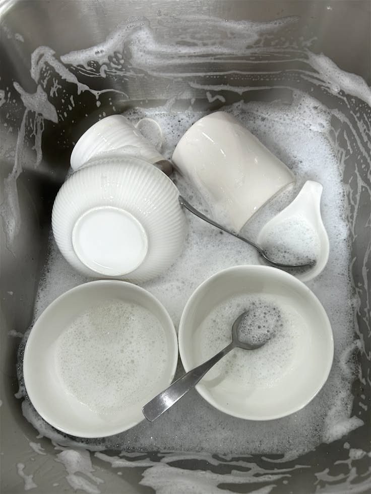 6 Aesthetic Cleaning Videos That Make Organizing Look Like Art 6 White ceramic bowls and metal spoons soaking in a sink filled with soapy white bubbles.
