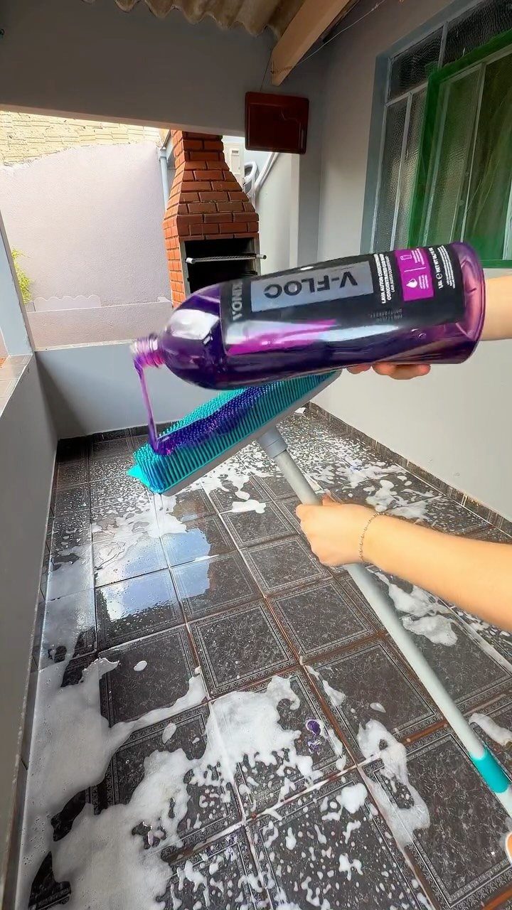 6 Aesthetic Cleaning Videos That Make Organizing Look Like Art 5 Hands pouring purple cleaning liquid onto a blue scrub brush on a soapy tiled floor.