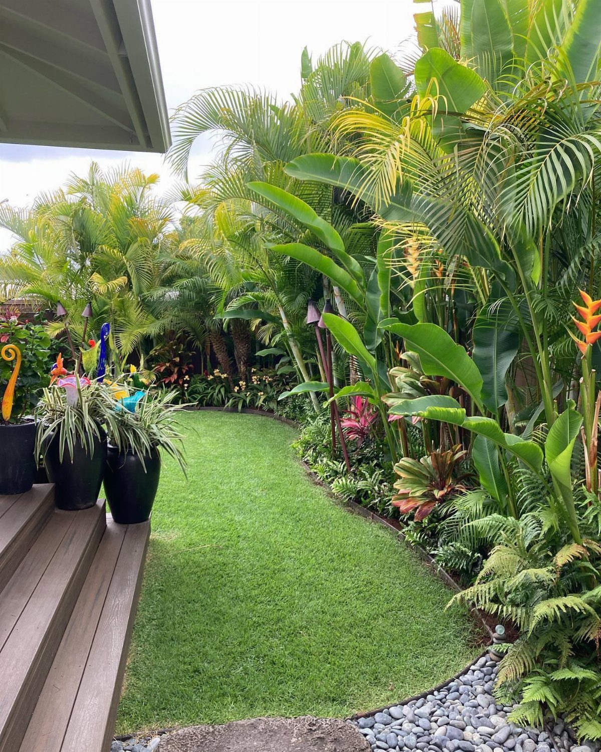 Lush tropical plants and a manicured green lawn bordering a wooden deck and stone path.
