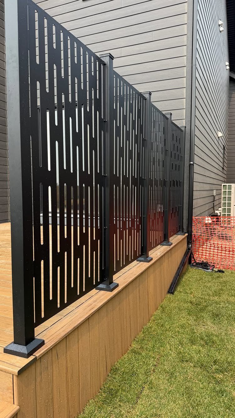 Black metal privacy screens with vertical slots installed along a wooden deck edge.