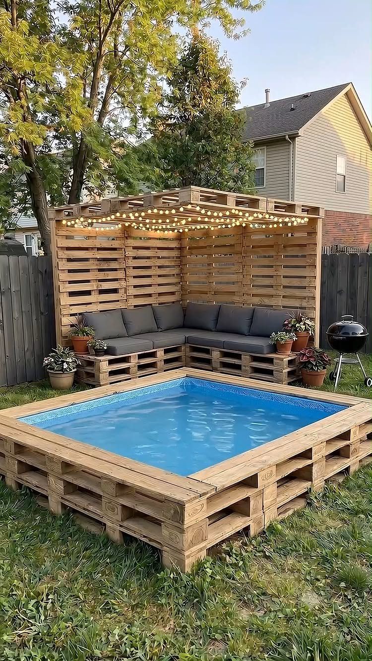 A backyard lounge area and small pool constructed from light-colored wooden pallets with string lights.