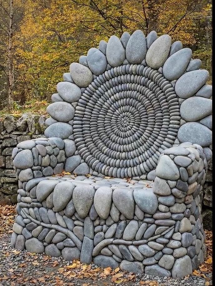 A large decorative chair made of smooth grey river stones arranged in intricate spiral and leaf patterns.