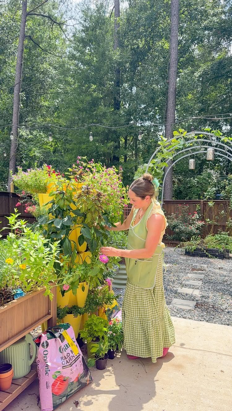 A woman tending to a tall yellow vertical planter filled with green plants and pink flowers.