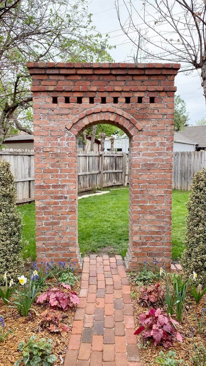 A red brick archway and a matching brick pathway in a green garden setting.