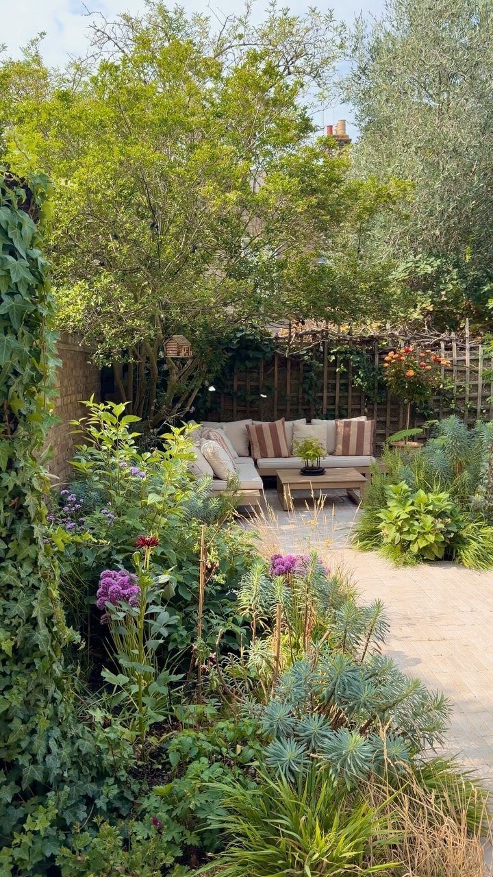 A cozy outdoor patio area surrounded by lush green plants and purple flowering shrubs.