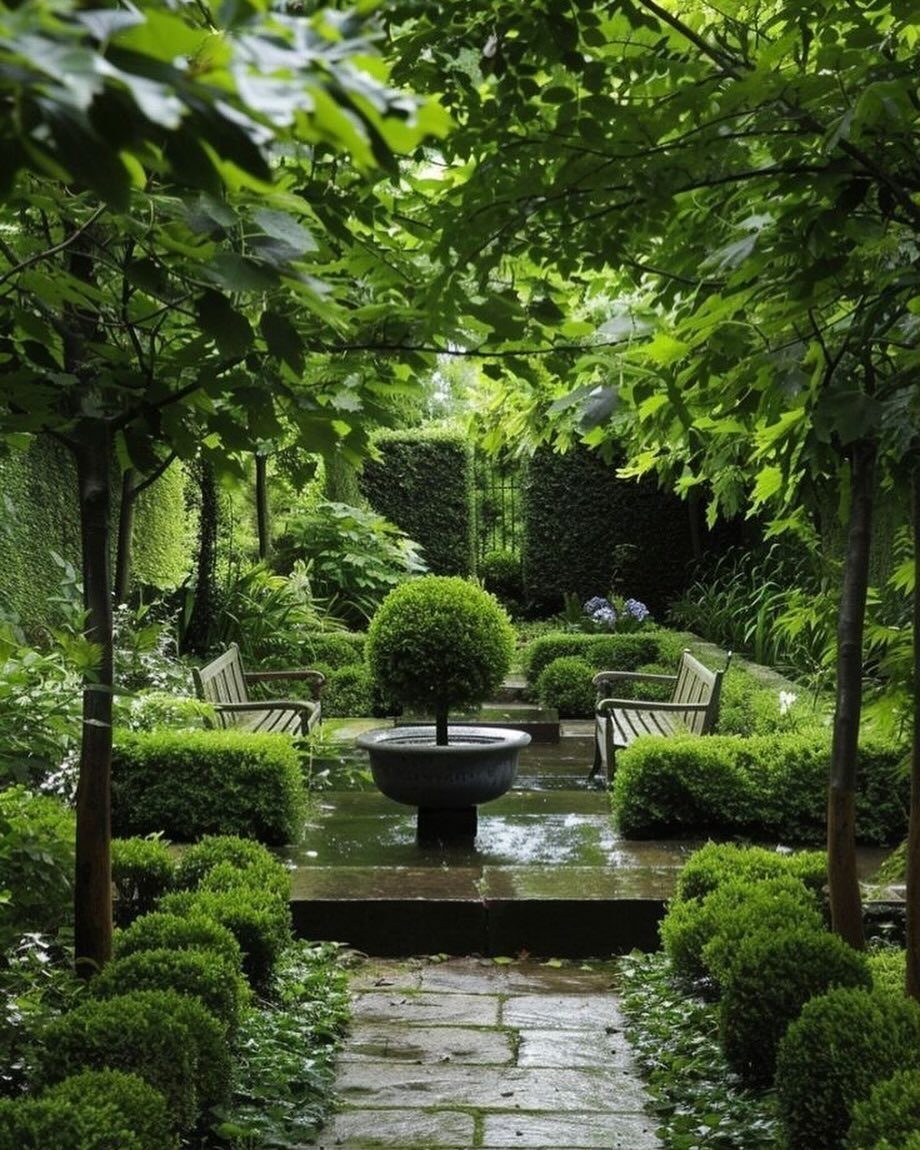 Wooden garden benches placed on a stone patio surrounded by lush green hedges and trees.