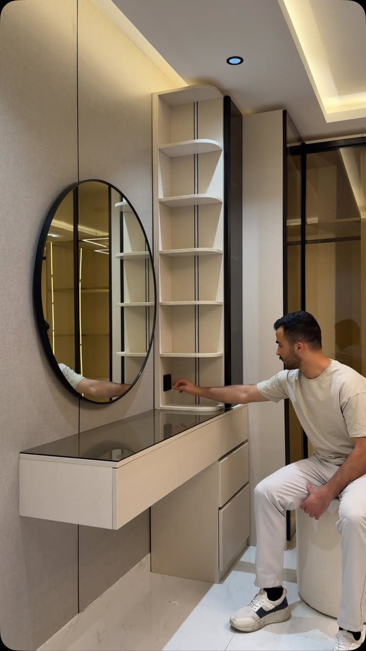 Man sitting on a white stool in a modern, minimalist walk-in closet with a vanity.