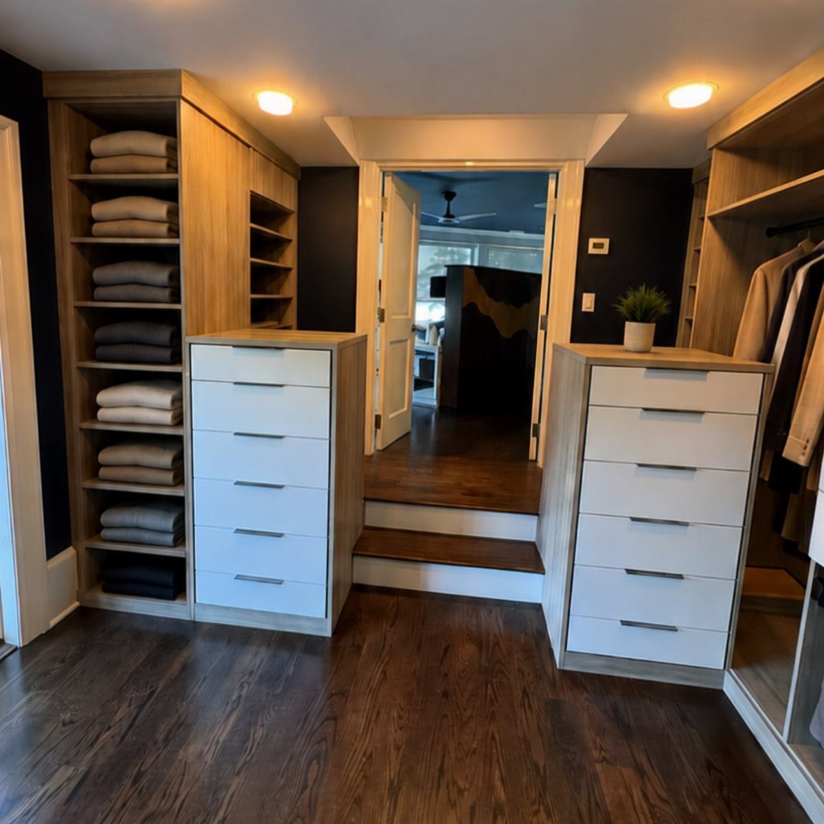 Dark wood flooring in a modern walk-in closet with light wood shelving and white drawers.