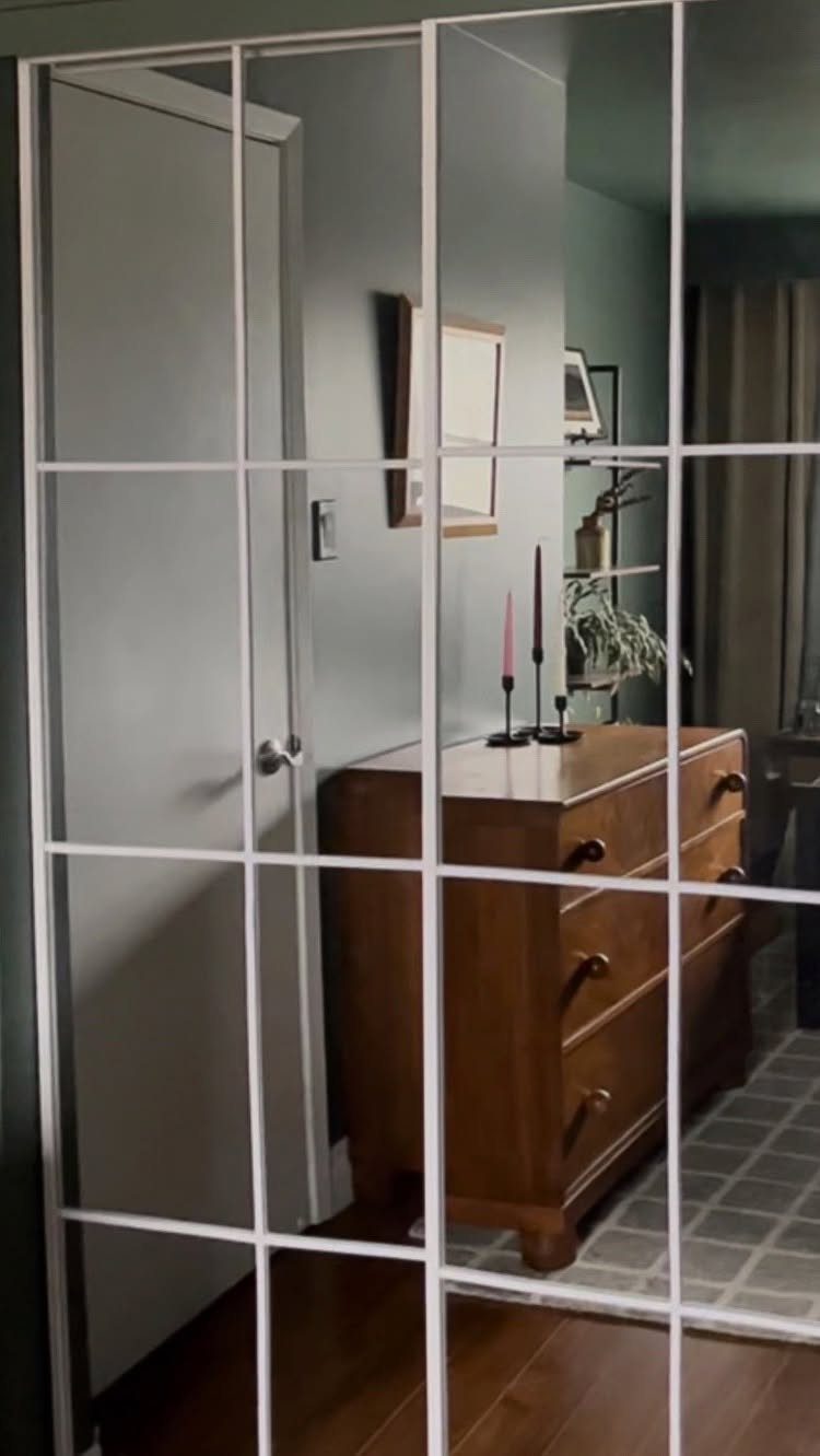 Full-length mirror with a white grid frame reflecting a wooden dresser and a blue wall.