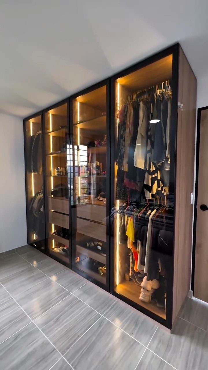 Modern built-in wardrobe with glass doors and warm interior LED lighting showing organized clothes.
