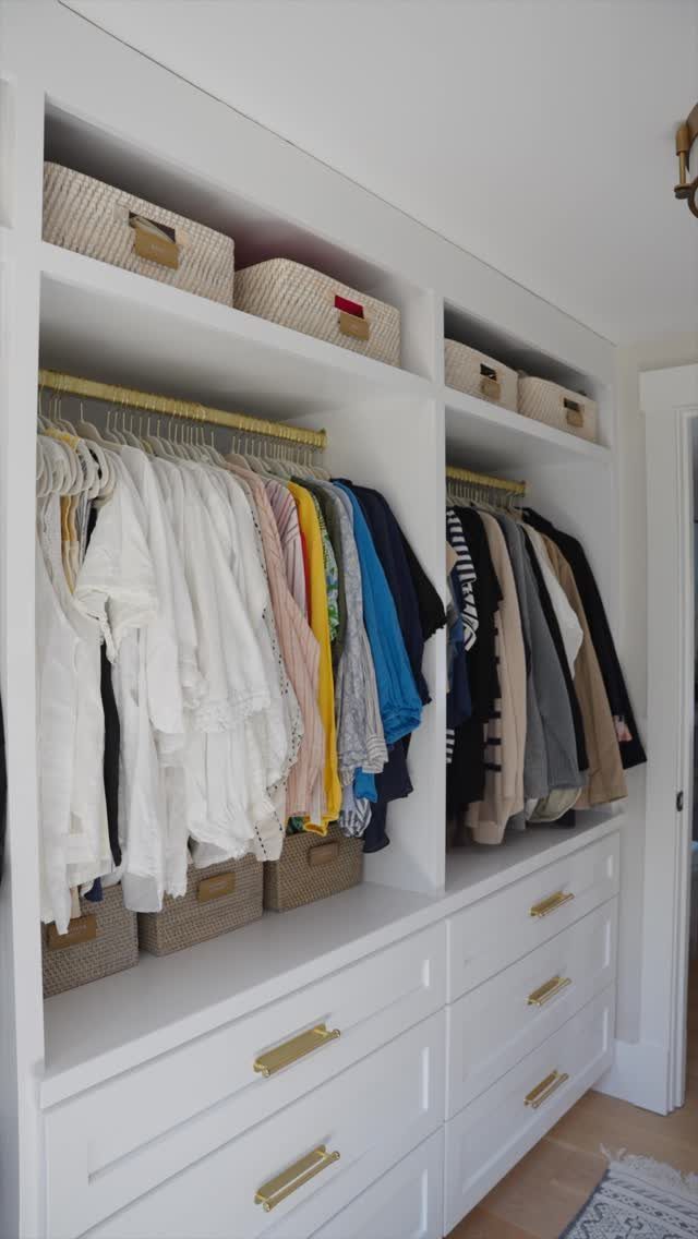White built-in closet with hanging clothes, drawers, and woven bins on high shelves.