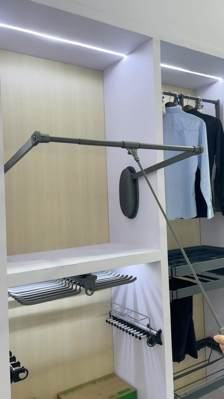 A grey pull-down closet rod mechanism extended from a white built-in closet system.