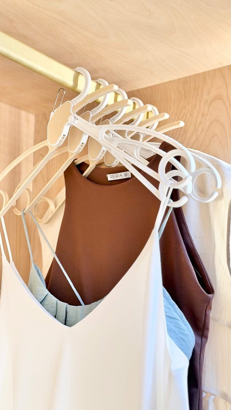 White plastic hangers holding various sleeveless tops on a gold closet rod.
