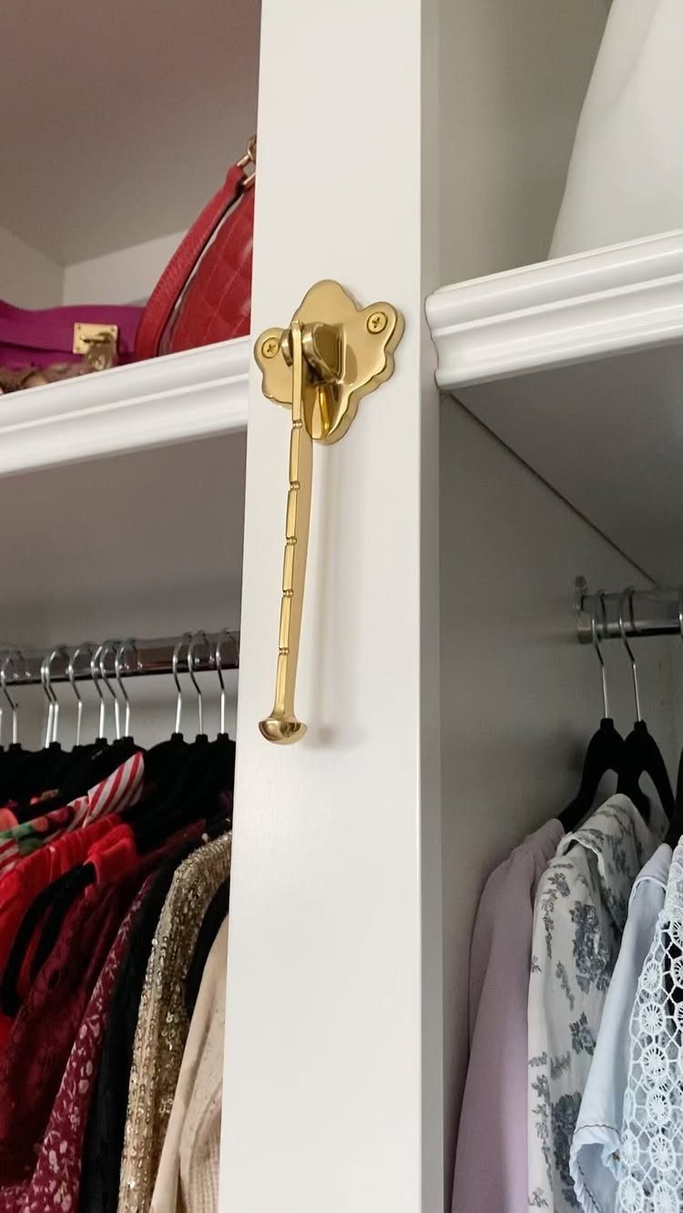A gold metal valet hook mounted on a white closet partition next to hanging clothes.