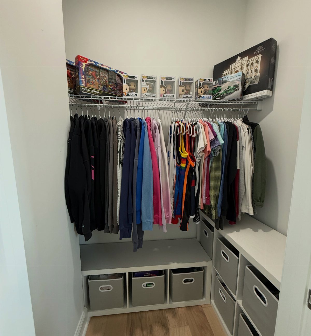 Hanging clothes on a rod beneath a wire shelf holding various toy boxes in a closet.