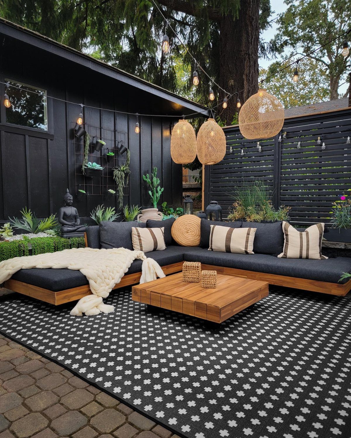 A black and white patterned outdoor rug under a wooden sectional sofa and coffee table.
