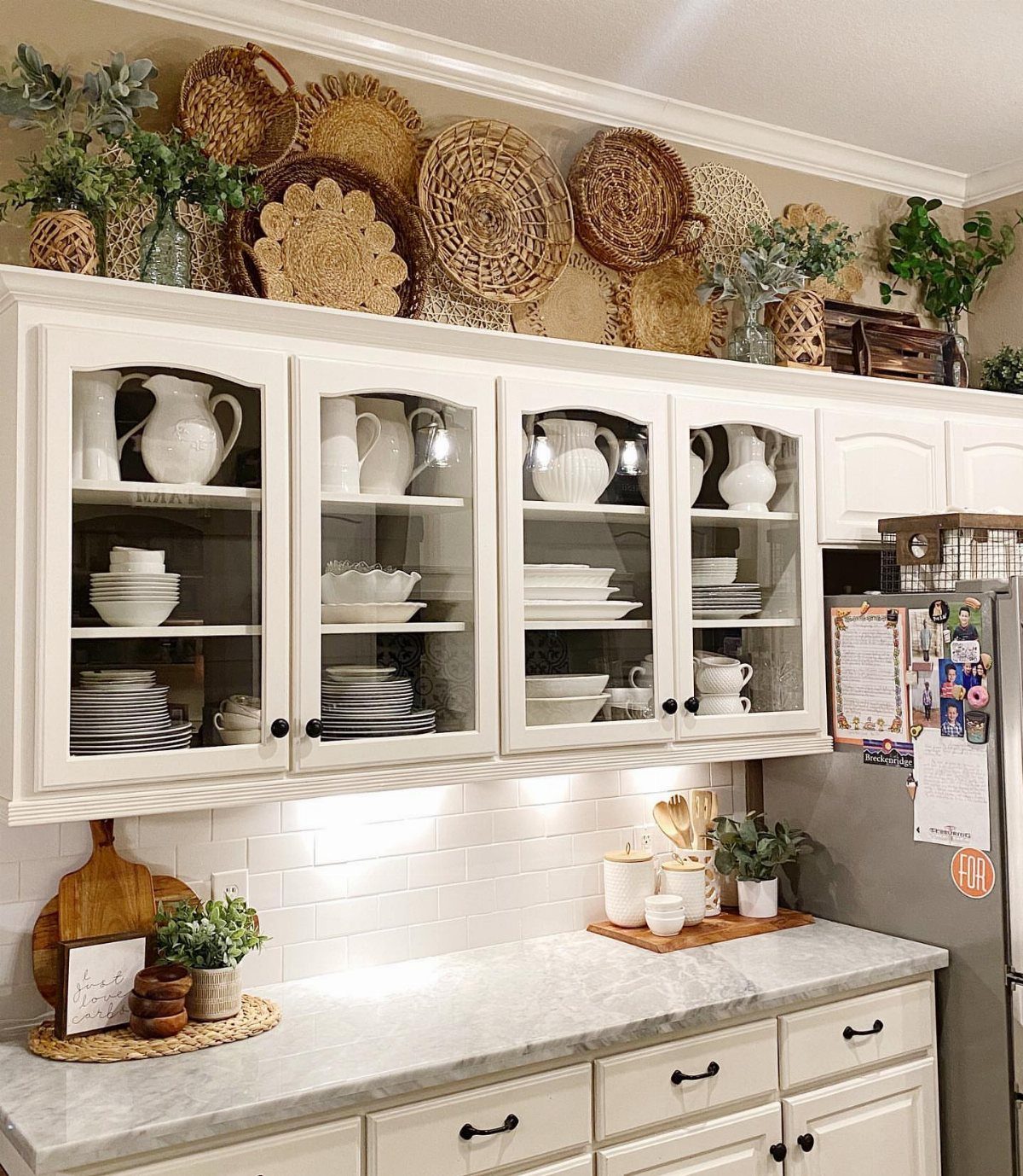 Woven wicker baskets and decorative trays arranged on top of white kitchen cabinets.