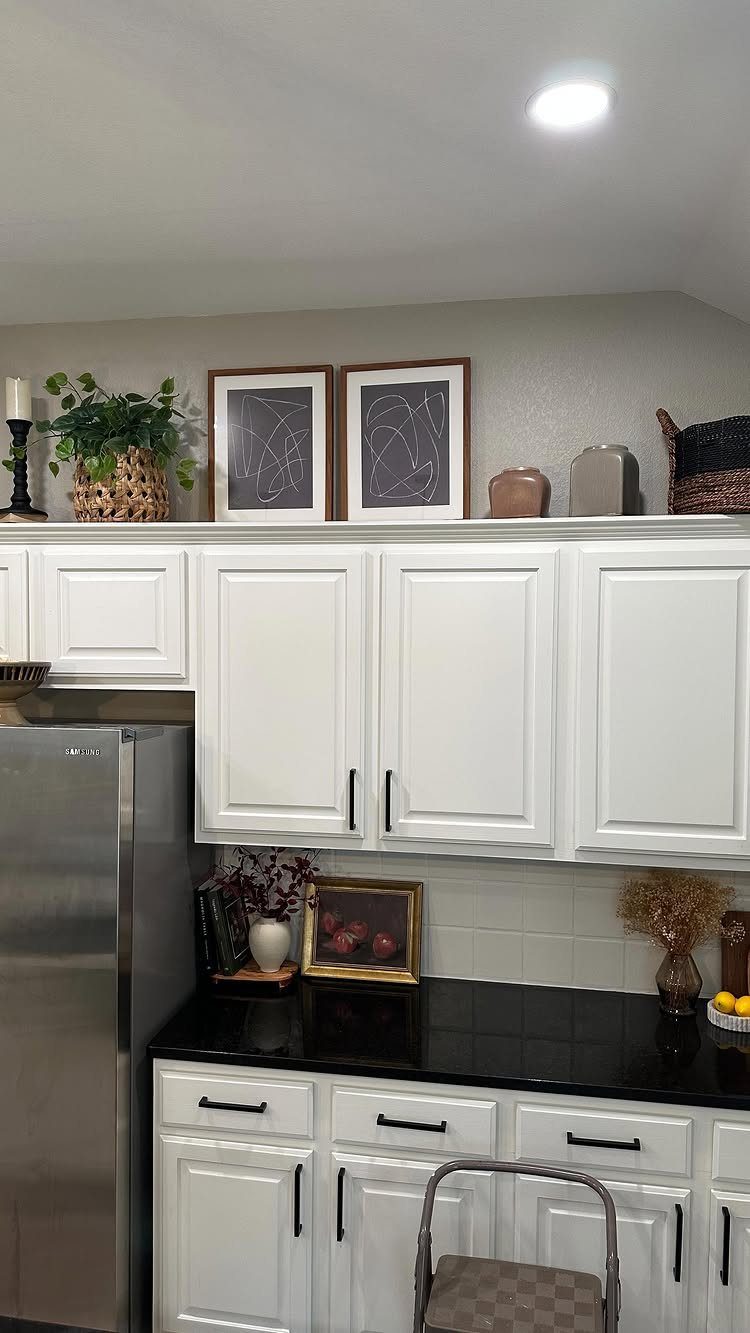 White kitchen cabinets decorated with framed art, a potted plant, and ceramic vases on top.