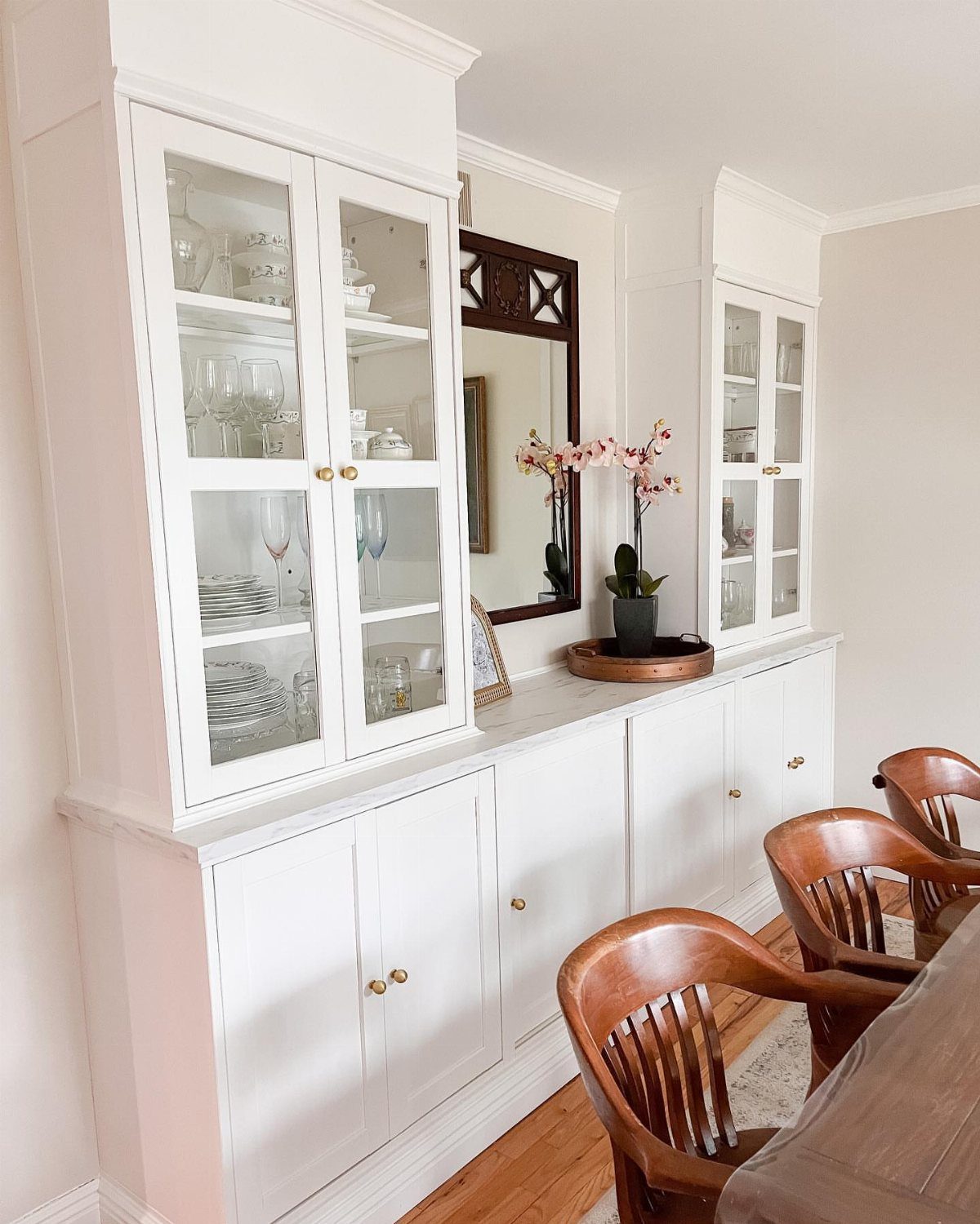 White built-in dining room cabinets with glass display doors and wooden chairs in the foreground.