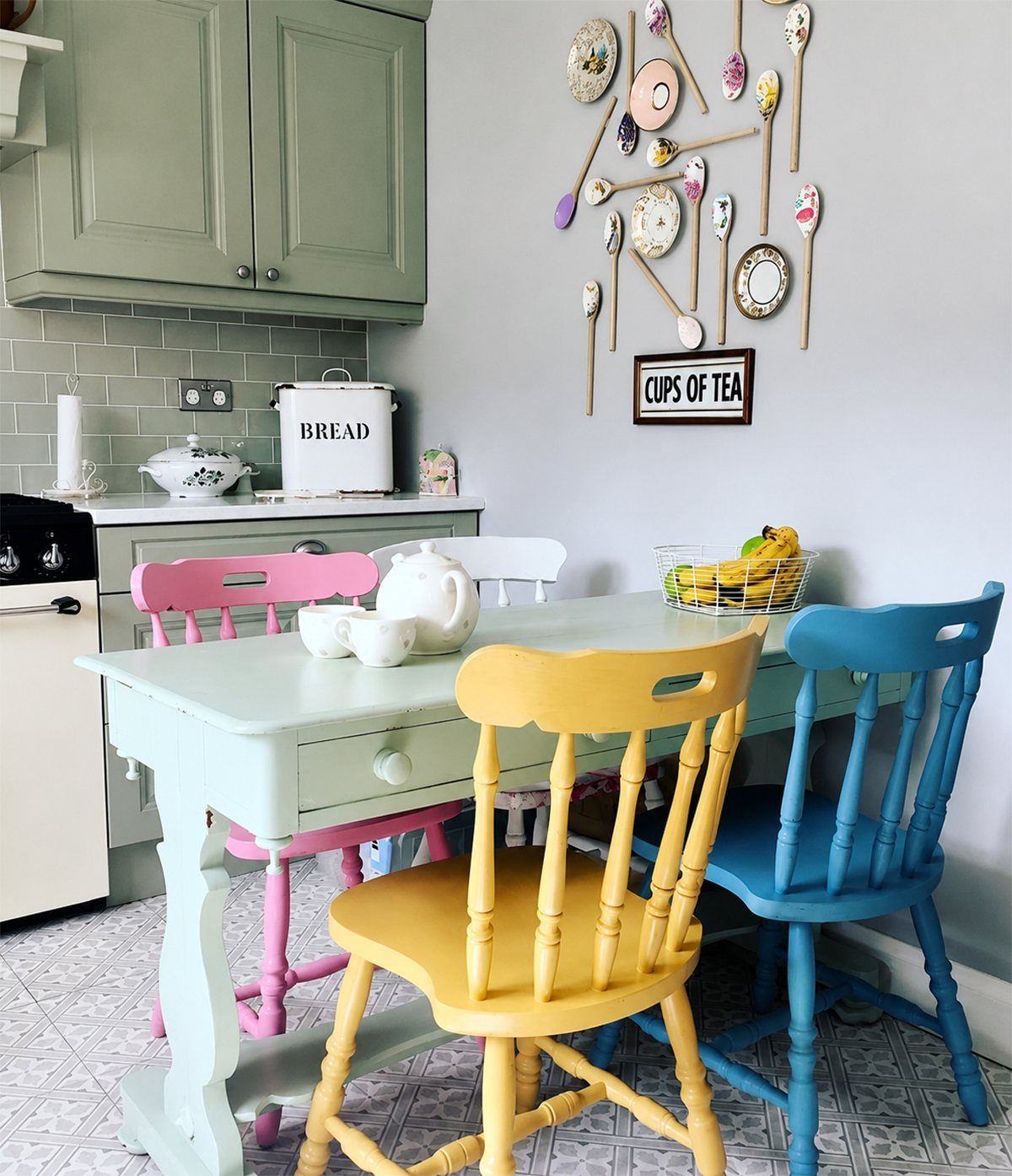 Colorful pink, yellow, and blue wooden chairs surrounding a light blue dining table in a kitchen.