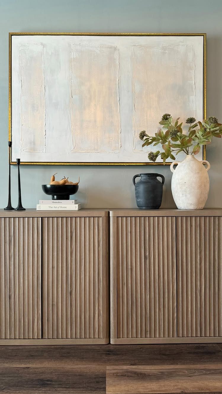 11 Minimalist Dining Room Decor Ideas for Calm, Collected Spaces 8 A fluted wooden sideboard decorated with vases, a black bowl, and large abstract wall art.