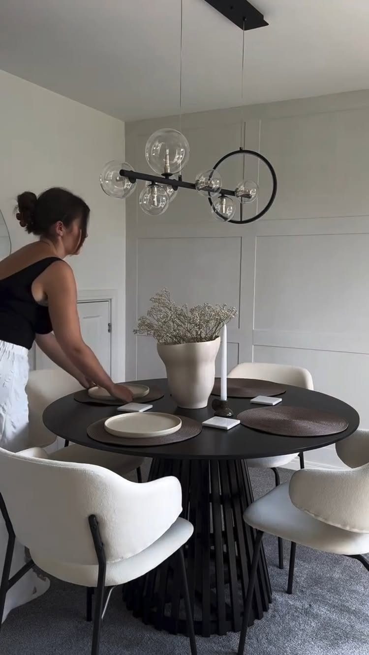 11 Minimalist Dining Room Decor Ideas for Calm, Collected Spaces 2 A woman setting a black minimalist dining table with white plates and dried flowers.