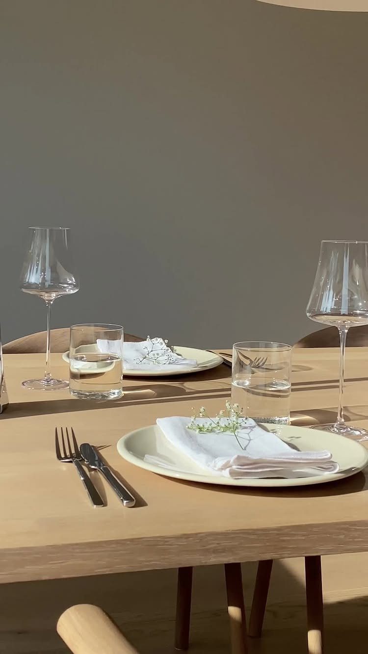 11 Minimalist Dining Room Decor Ideas for Calm, Collected Spaces 4 Minimalist table setting with white plates, linen napkins, clear glassware, and small flowers on a wooden table.