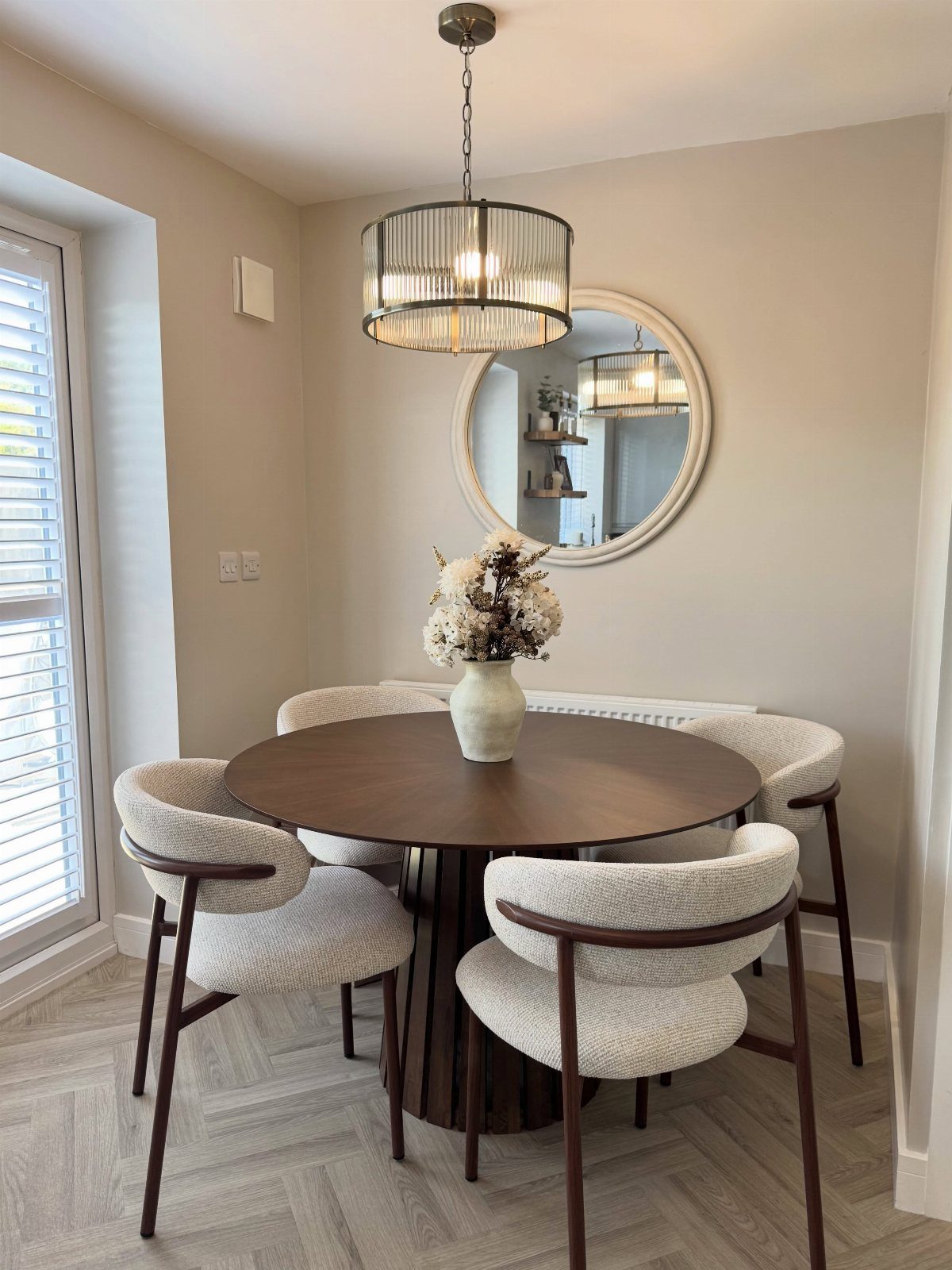 11 Minimalist Dining Room Decor Ideas for Calm, Collected Spaces 1 A round dark wood dining table with cream chairs and a drum pendant light in a neutral room.