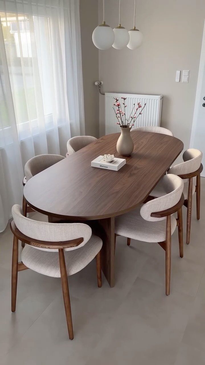 11 Minimalist Dining Room Decor Ideas for Calm, Collected Spaces 9 Oval wooden dining table with cream chairs and globe pendant lights in a minimalist room.