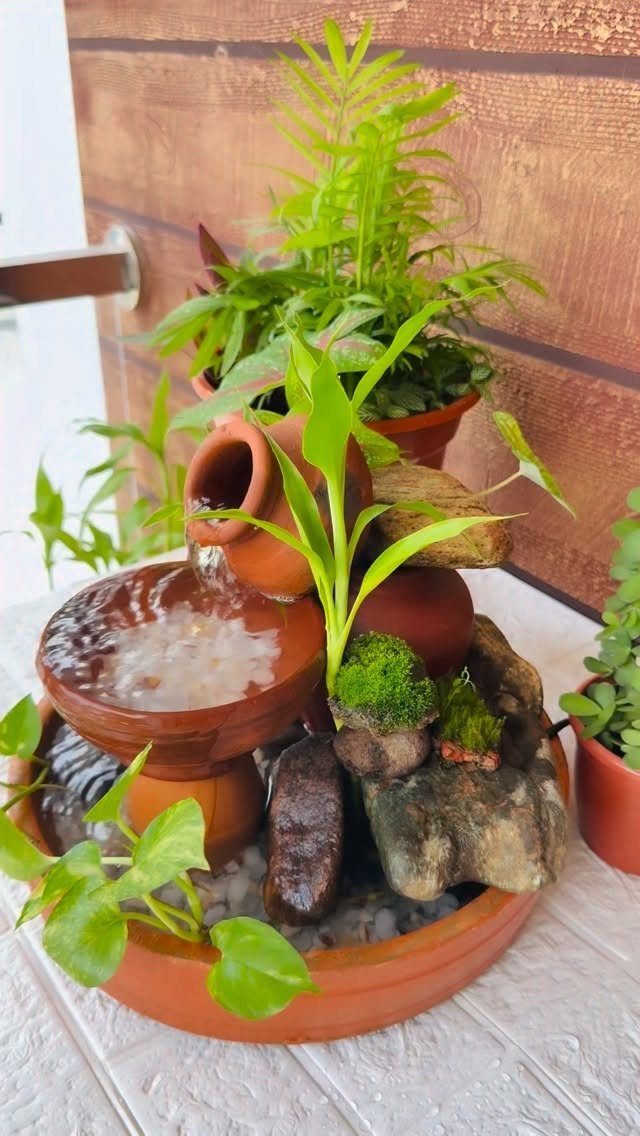 A small terracotta pot water fountain with flowing water, green plants, and decorative rocks.