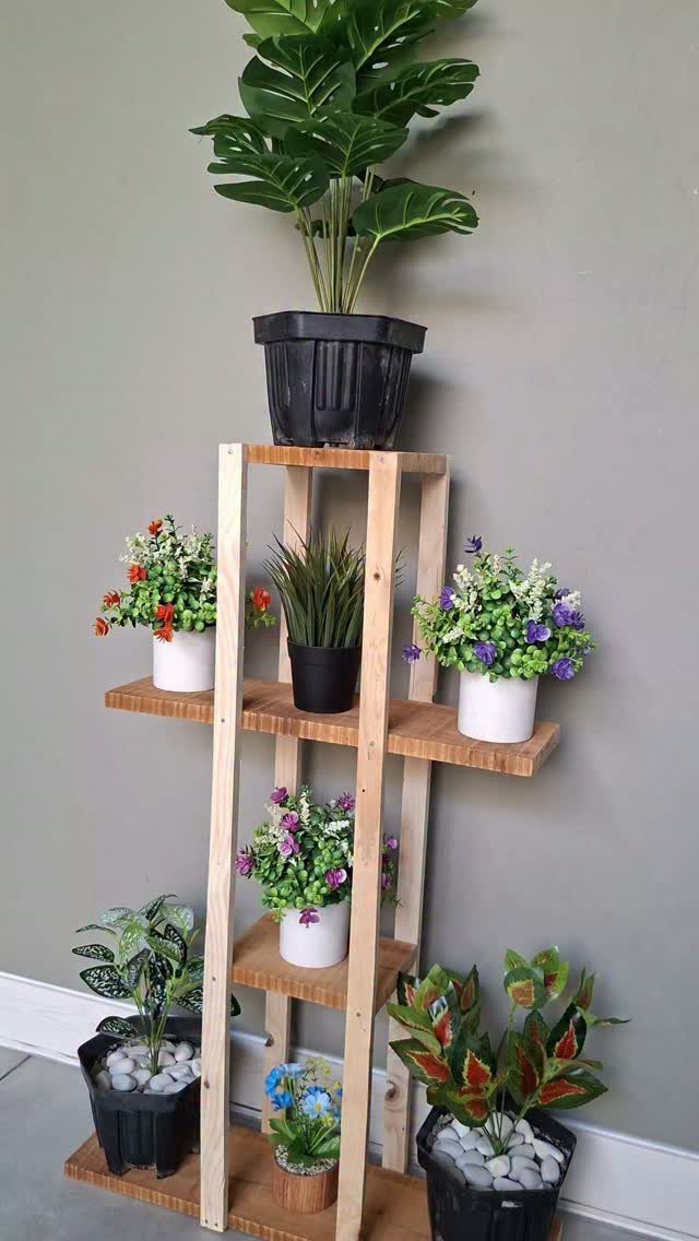 DIY Plant Stand Indoor: 5 Ideas With Driftwood, Ladders and Tiered Wood 3 A wooden multi-tiered plant stand holding various small potted flowering plants against a grey wall.
