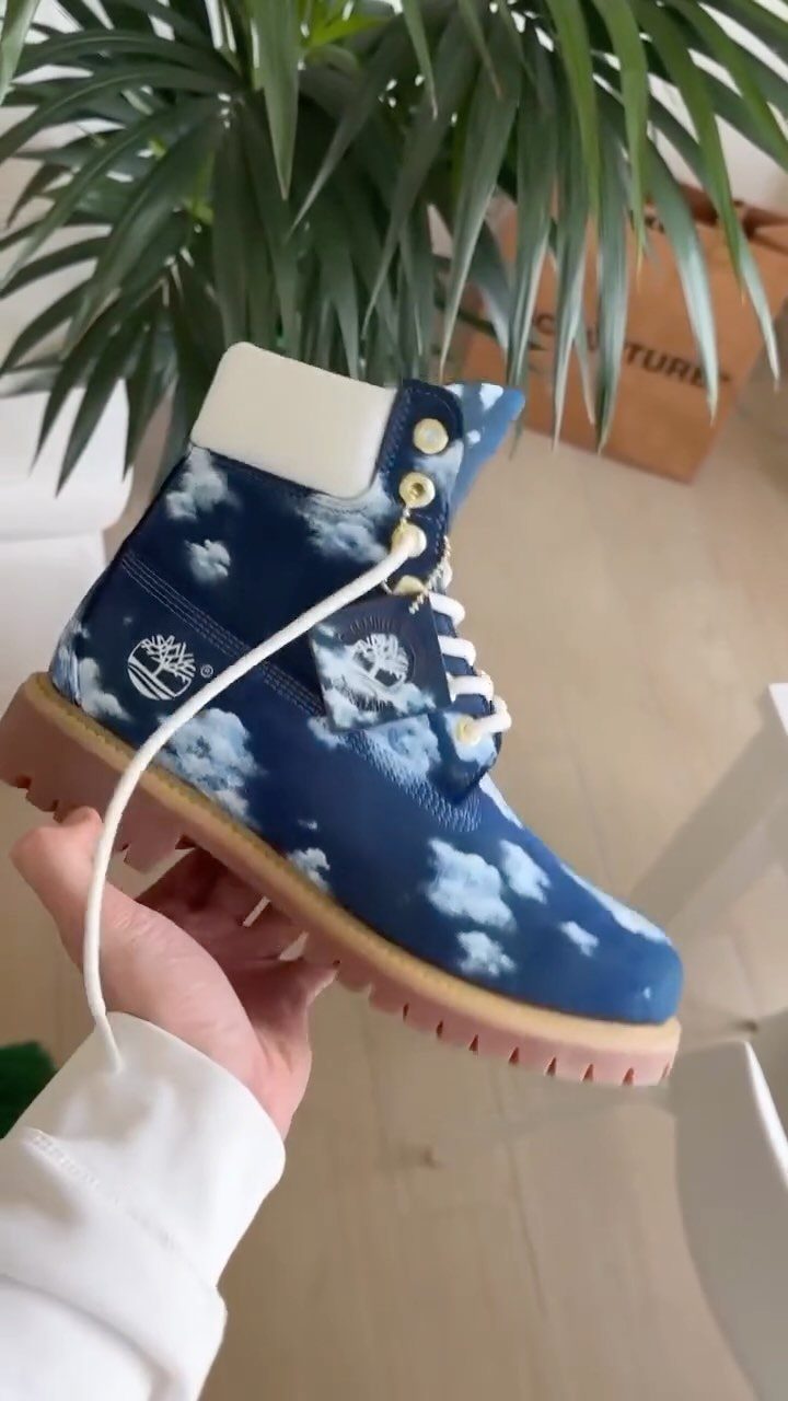A blue high-top boot with white cloud patterns held by a hand.