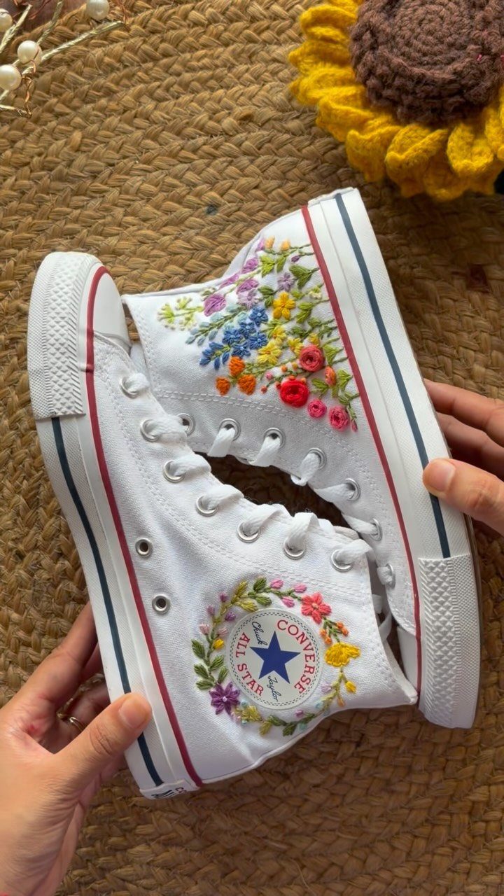 White canvas high-top sneakers decorated with colorful embroidered floral patterns held by hands.