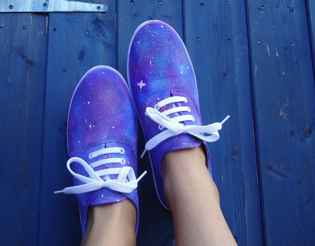 Galaxy painted purple and blue canvas sneakers with white laces on a blue wooden surface.