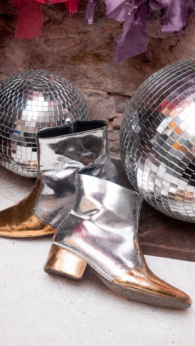 Silver metallic ankle boots with gold toes sitting next to two disco balls.