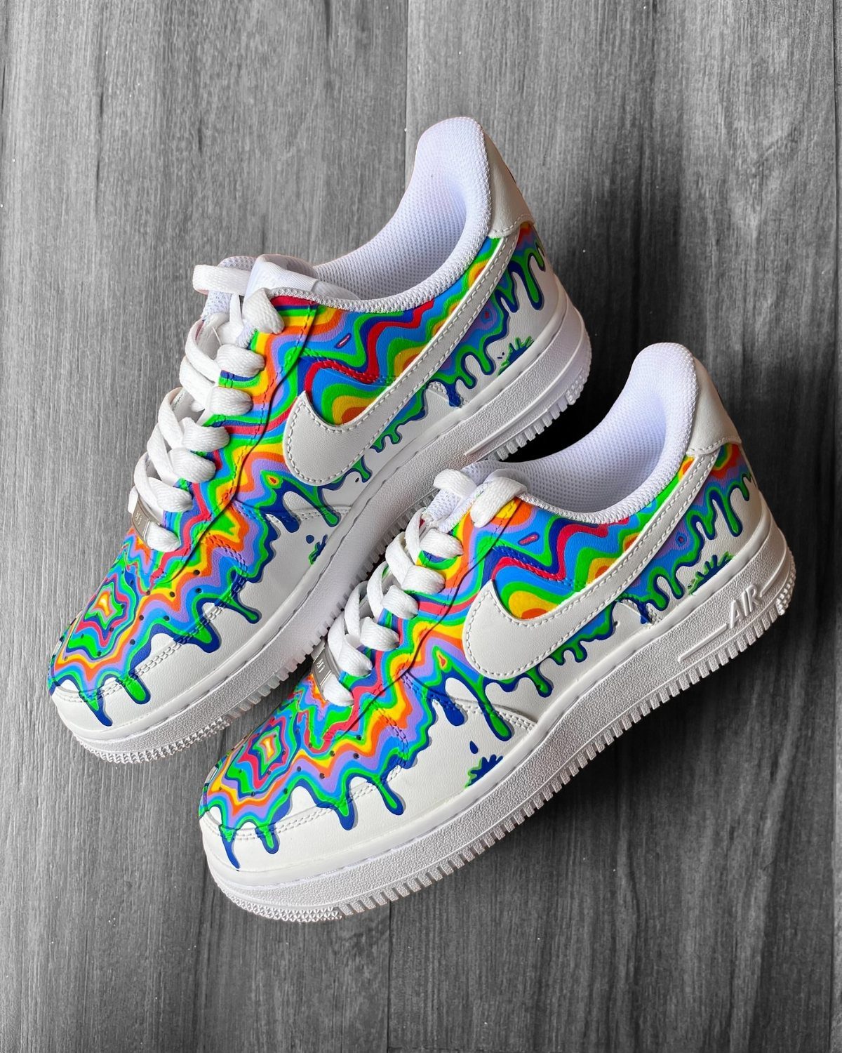 White Nike sneakers featuring vibrant, wavy rainbow patterns and colorful dripping paint designs.