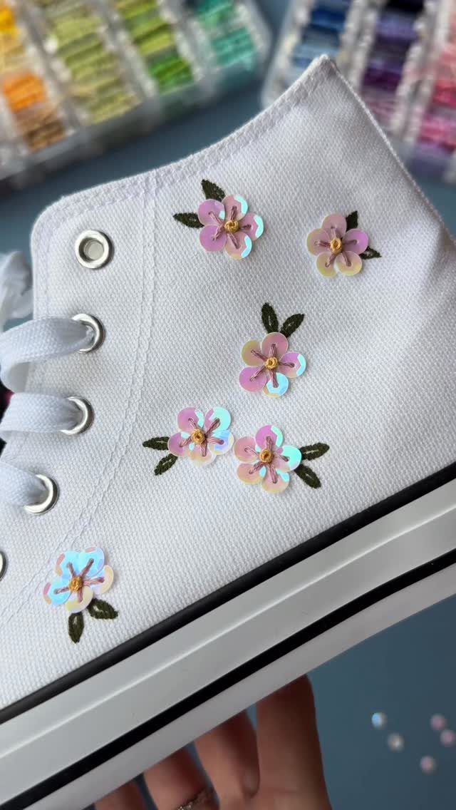 White canvas high-top sneaker decorated with small, colorful sequined flower patches and green leaves.