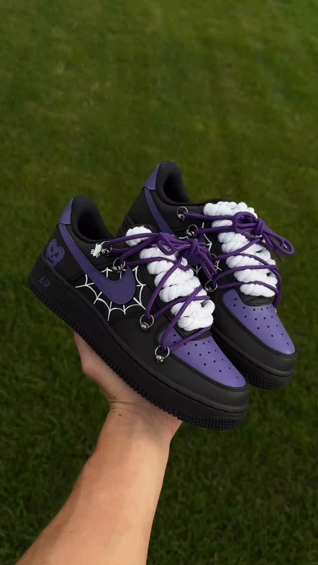 A hand holding custom black and purple Nike sneakers with spiderweb designs.