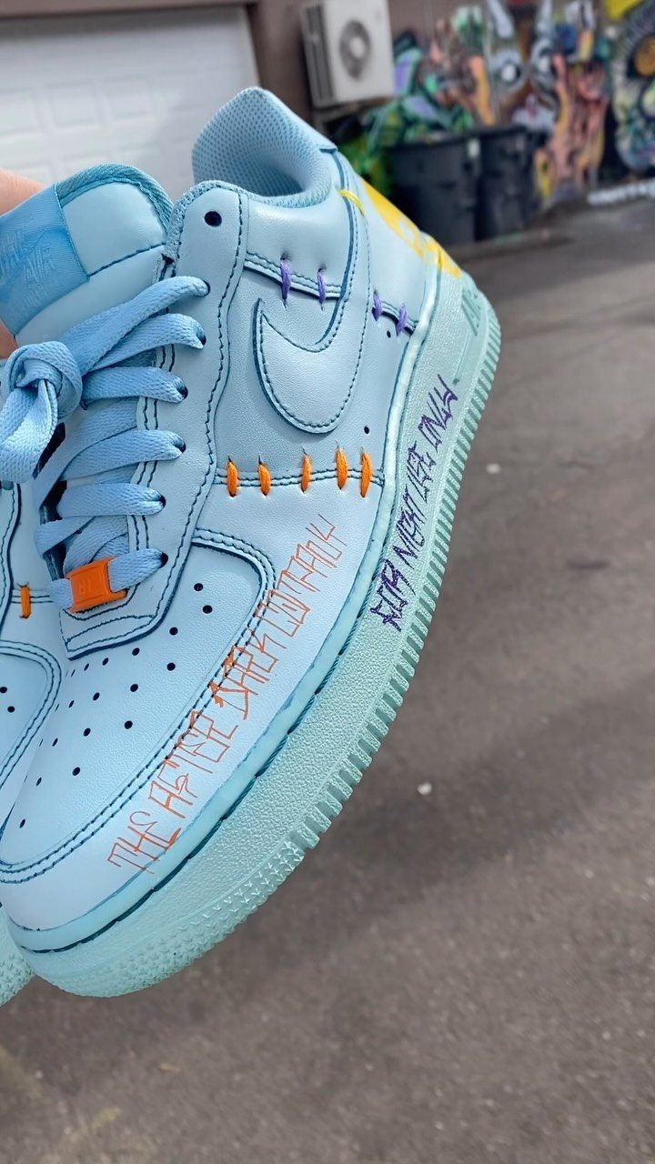 Light blue Nike sneaker with orange stitching and handwritten text being held outdoors.