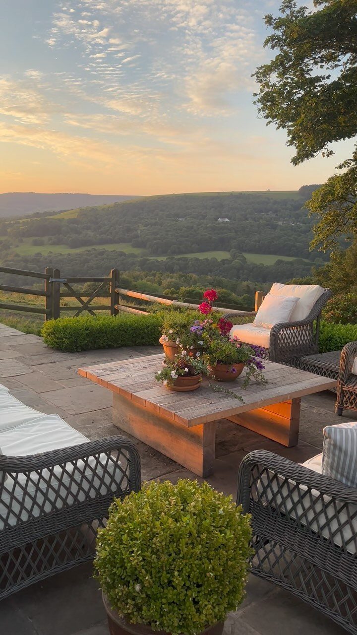 Dream Garden for Your Aesthetic: 20 Ideas to Steal 1 Stone patio with wicker furniture and potted flowers overlooking a scenic green valley at sunset.