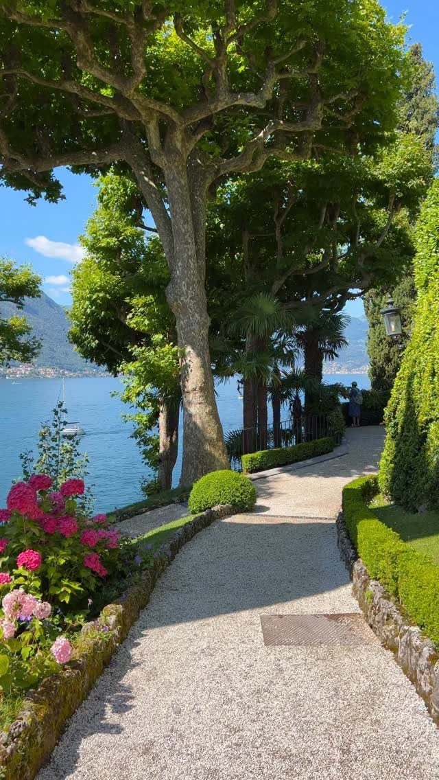 Dream Garden for Your Aesthetic: 20 Ideas to Steal 12 A gravel garden path lined with green hedges and pink flowers overlooking a blue lake.