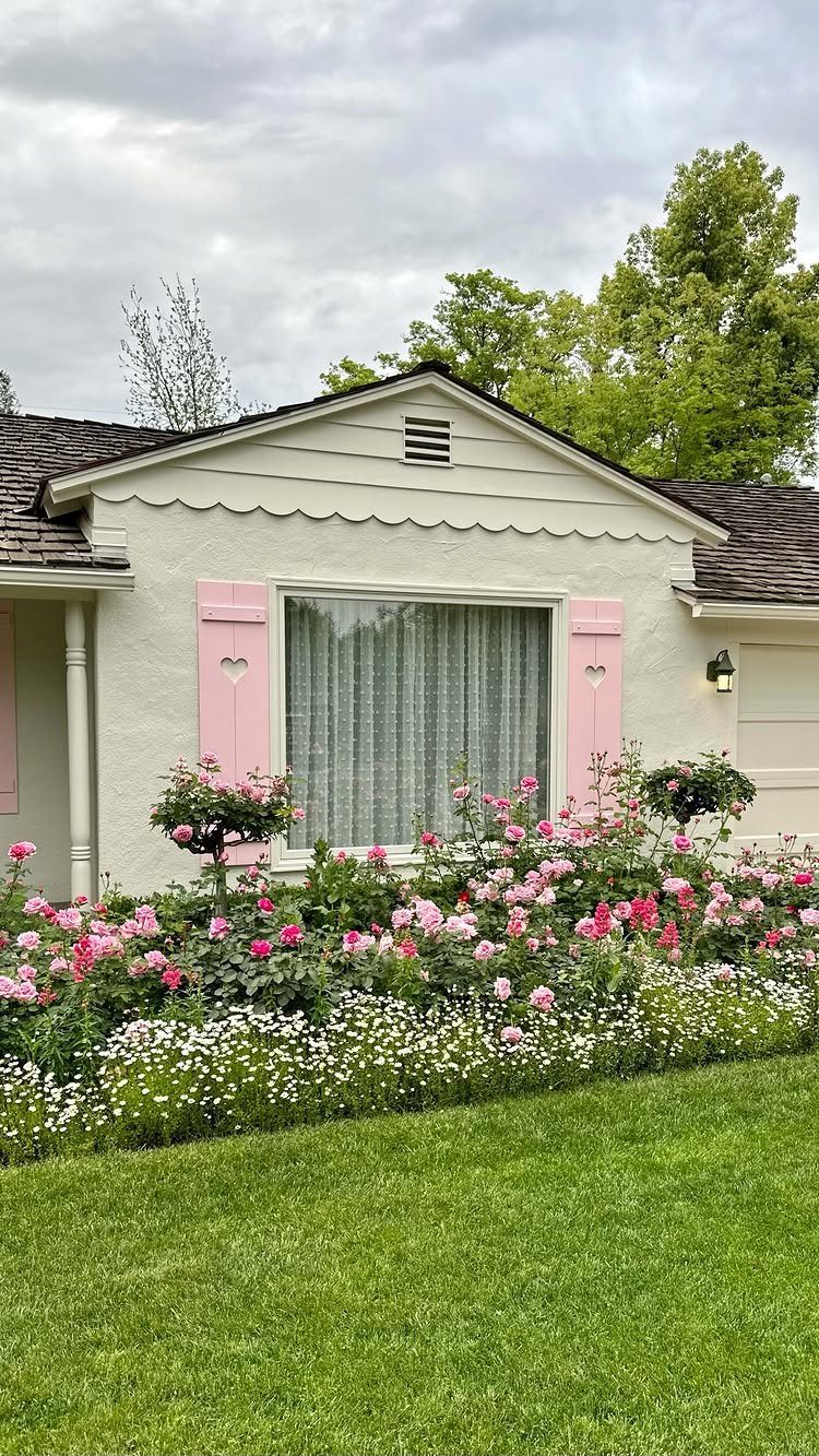 Dream Garden for Your Aesthetic: 20 Ideas to Steal 5 Pink roses and white flowers blooming in front of a white cottage with pink shutters.