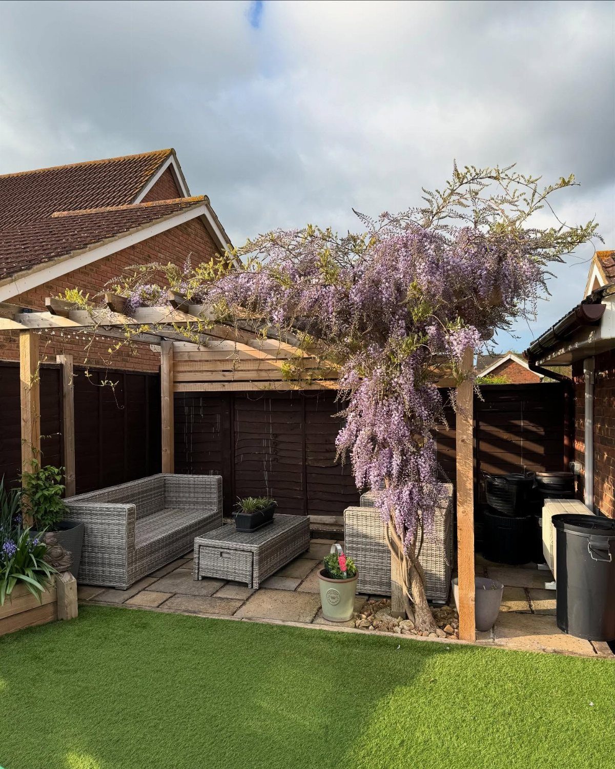 Dream Garden for Your Aesthetic: 20 Ideas to Steal 4 Purple wisteria flowers cascading over a wooden pergola with grey wicker patio furniture.