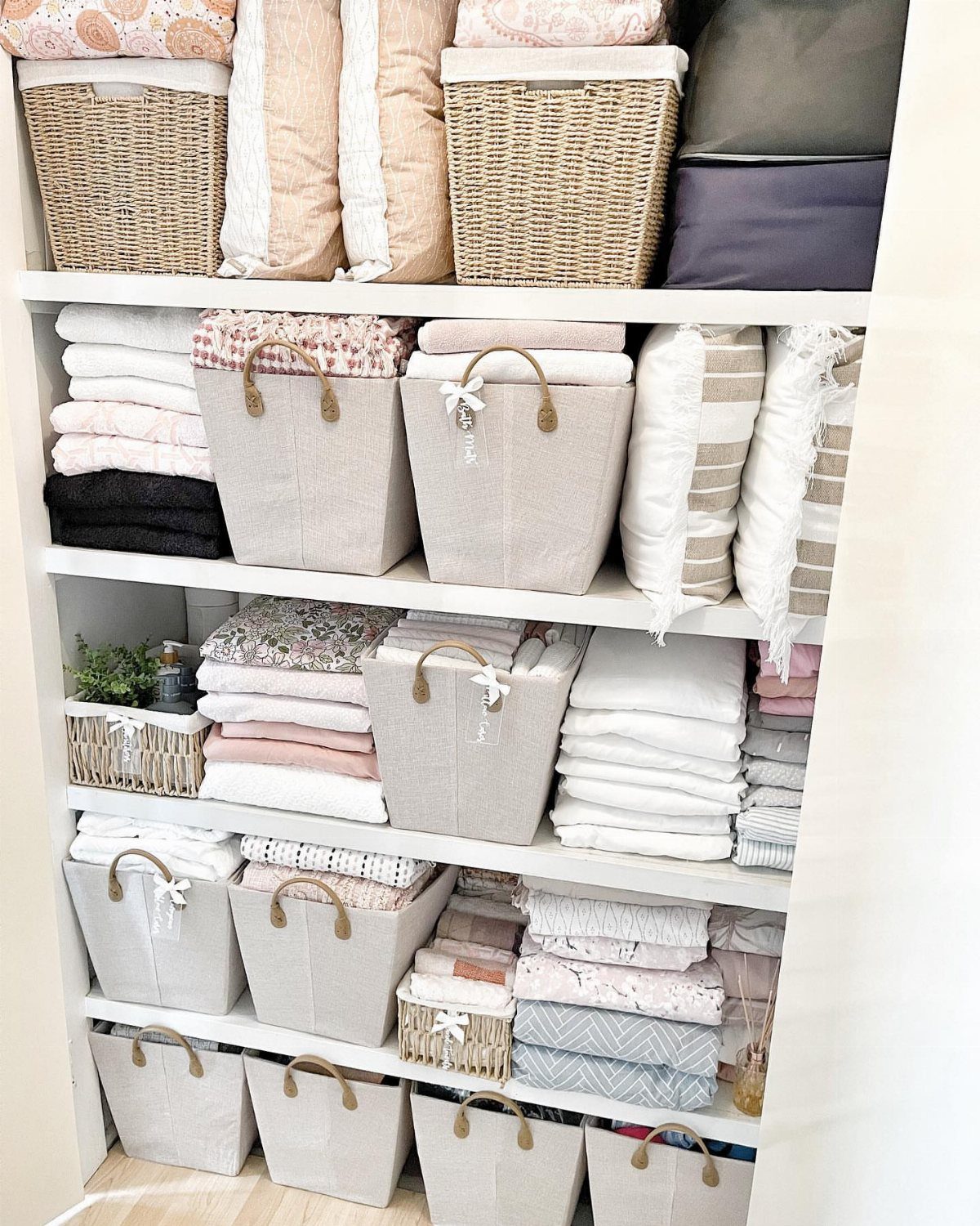 White shelves holding numerous fabric and wicker baskets filled with neatly folded linens and pillows.