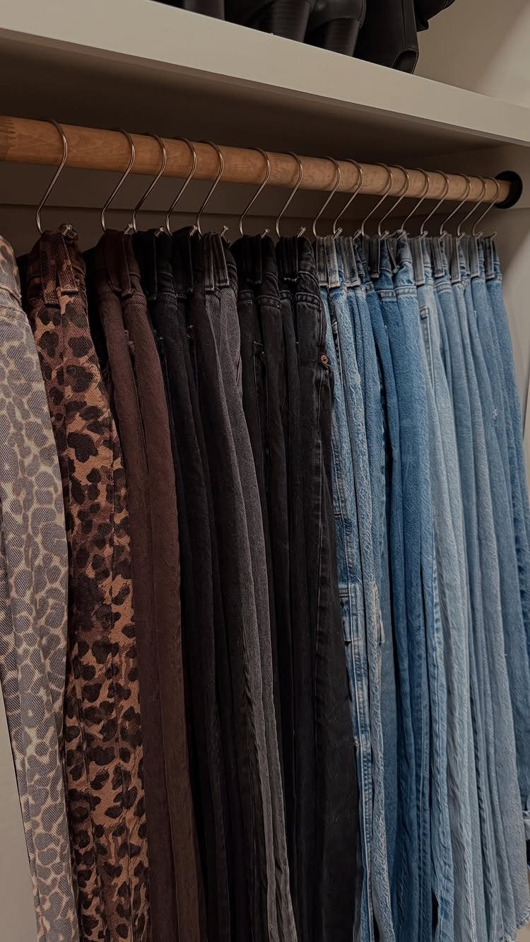 Various styles of pants hanging from silver S hooks on a wooden closet rod.