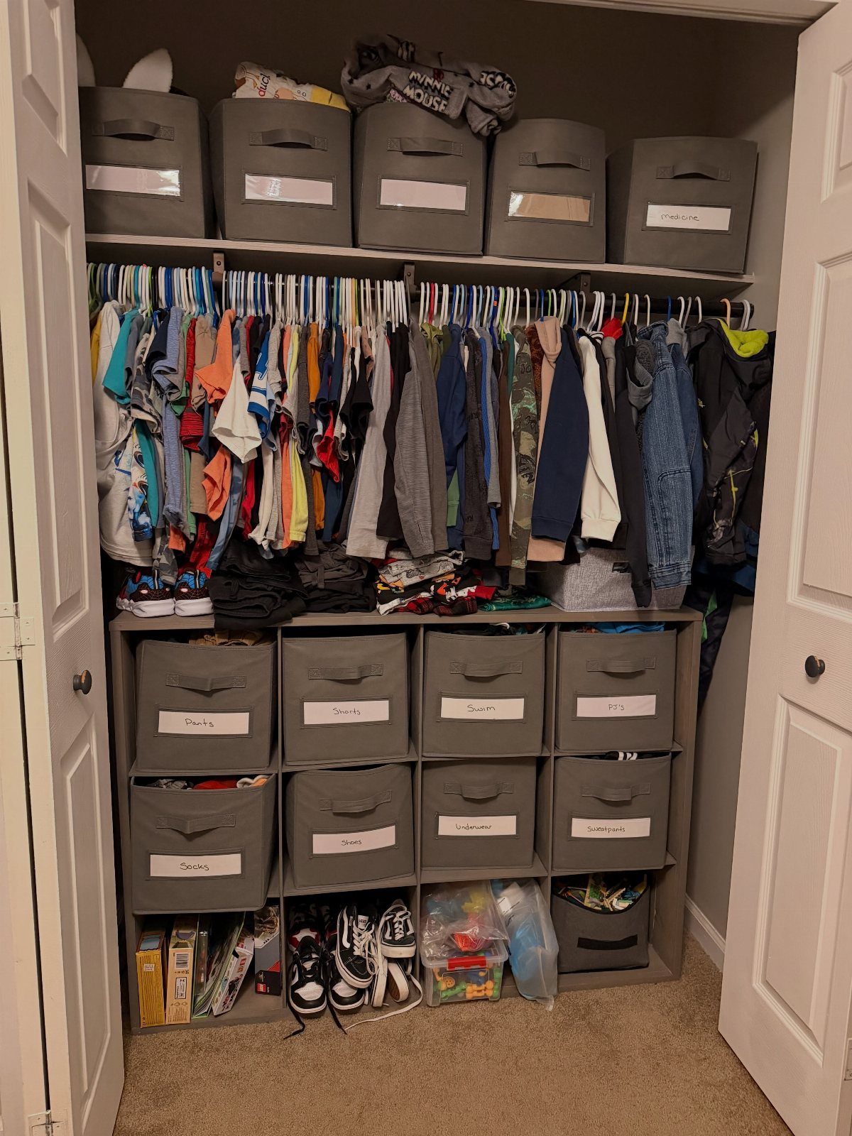 Grey fabric storage bins with white labels arranged on closet shelves and in cubbies.
