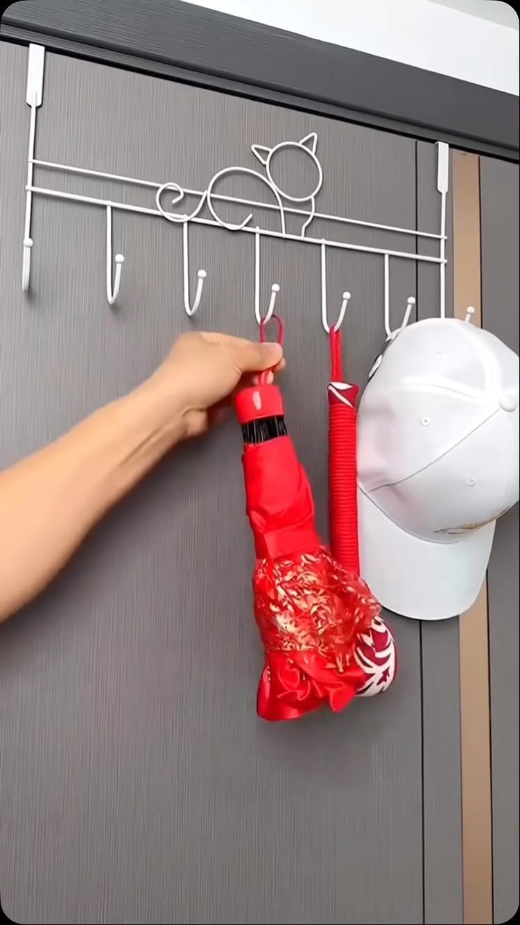 A hand hangs a red stocking onto a white cat-shaped over-the-door hook rack.