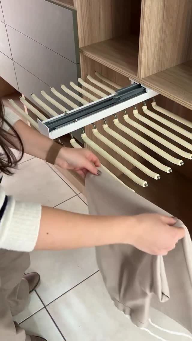 Hands placing beige clothing onto a white pull-out closet storage rack system.